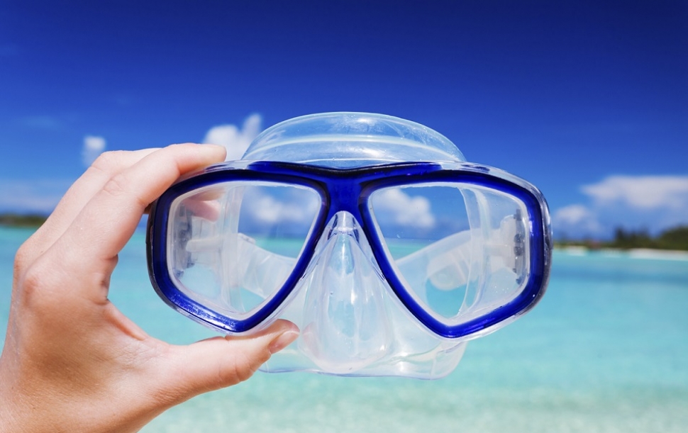 Hand holding snorkel googles against beach and sky